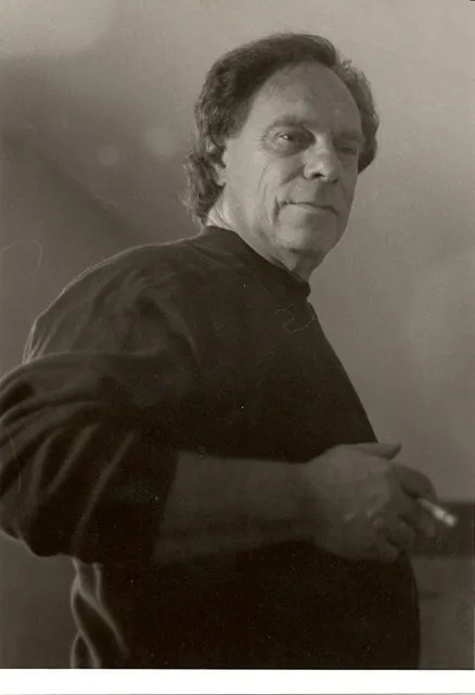 A man in black shirt holding cigarette and looking at camera.